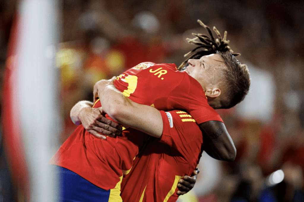 Two male football players embracing, they are wearing red shirts with yellow text and blue shorts